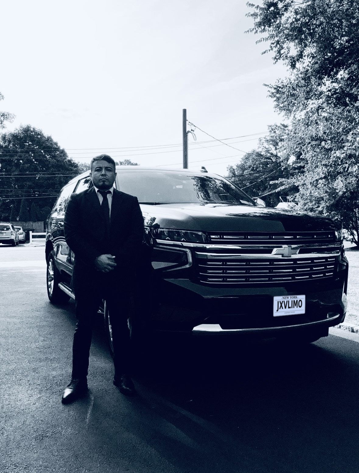 John V., owner of JXV Limo Services, standing in a suit beside a JXV Chevrolet Suburban